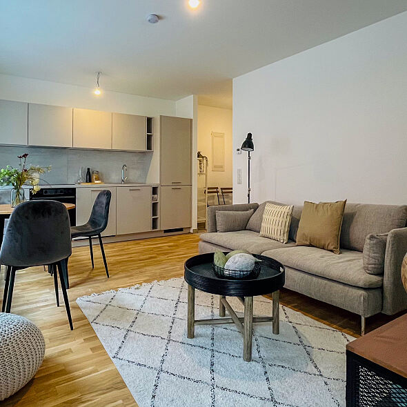 Die Wohnküche des „Kh:Ek:51“ bietet einen nahtlosen Übergang vom Kochbereich zum entspannenden Wohnbereich mit Sofa.